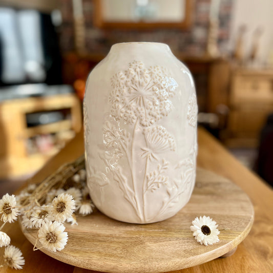 White embossed vase on a wooden surface with flowers