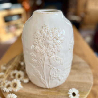 White textured vase on a wooden surface with small white flowers
