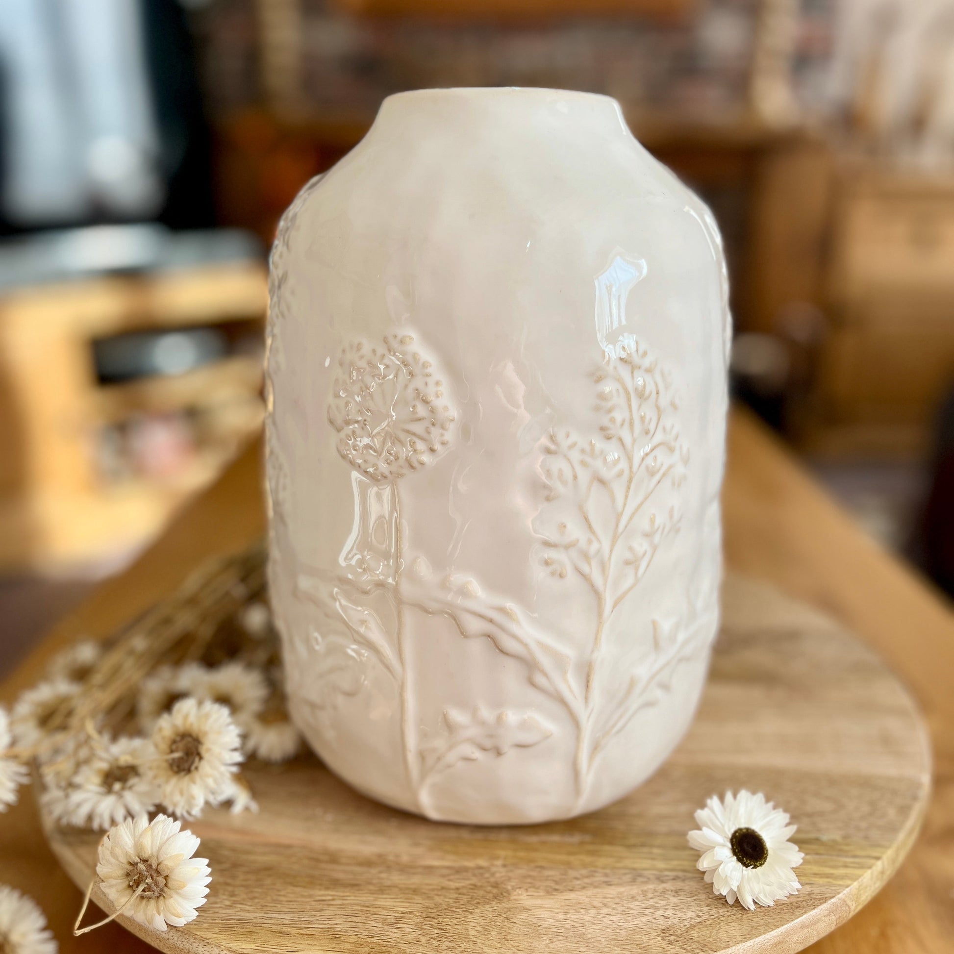 Decorative white vase with flower embossment on a wooden surface with flowers.