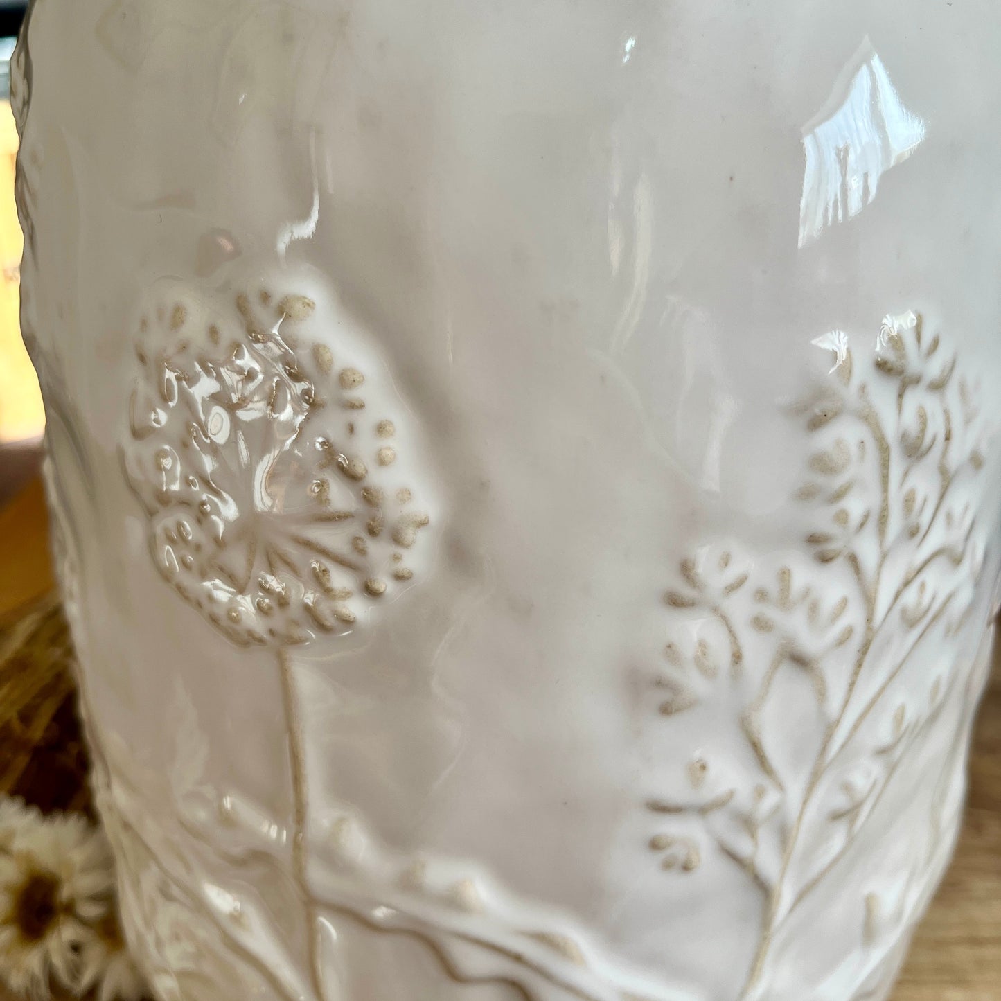 Close up white ceramic vase with floral embossing on a wooden surface