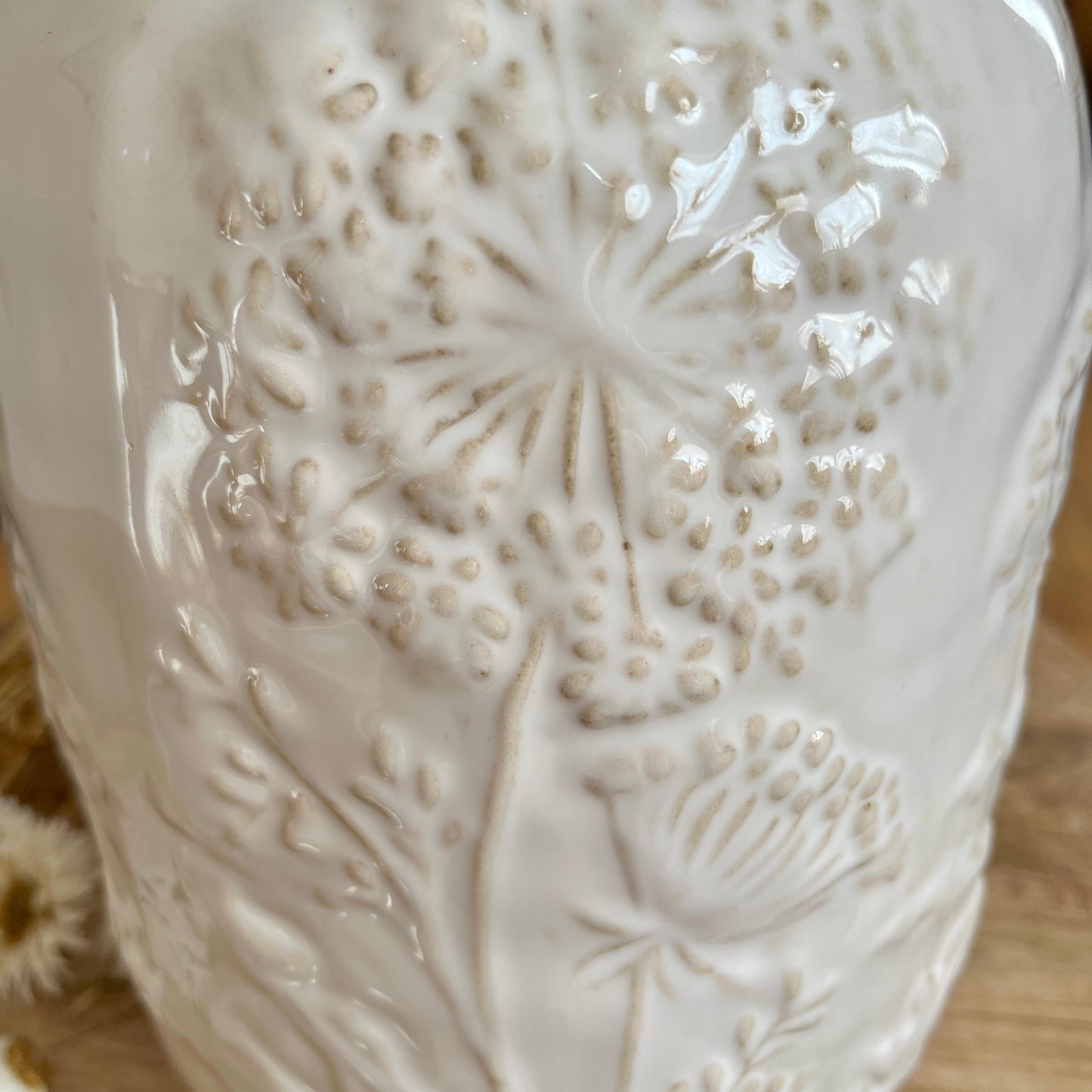 Close up of white ceramic vase with floral embossing on a wooden surface