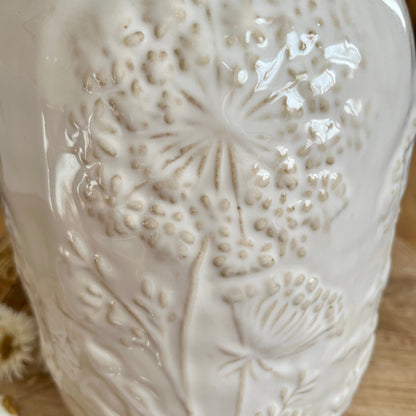 Close up of white ceramic vase with floral embossing on a wooden surface
