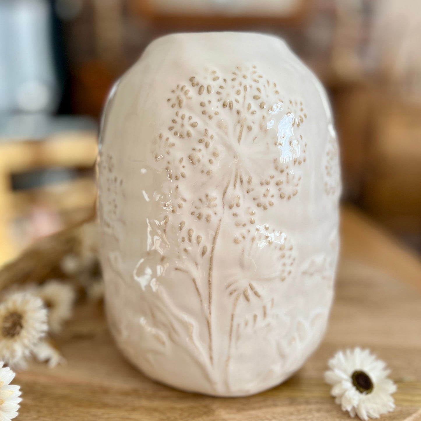 Close up of white ceramic vase with floral patterns on a wooden surface
