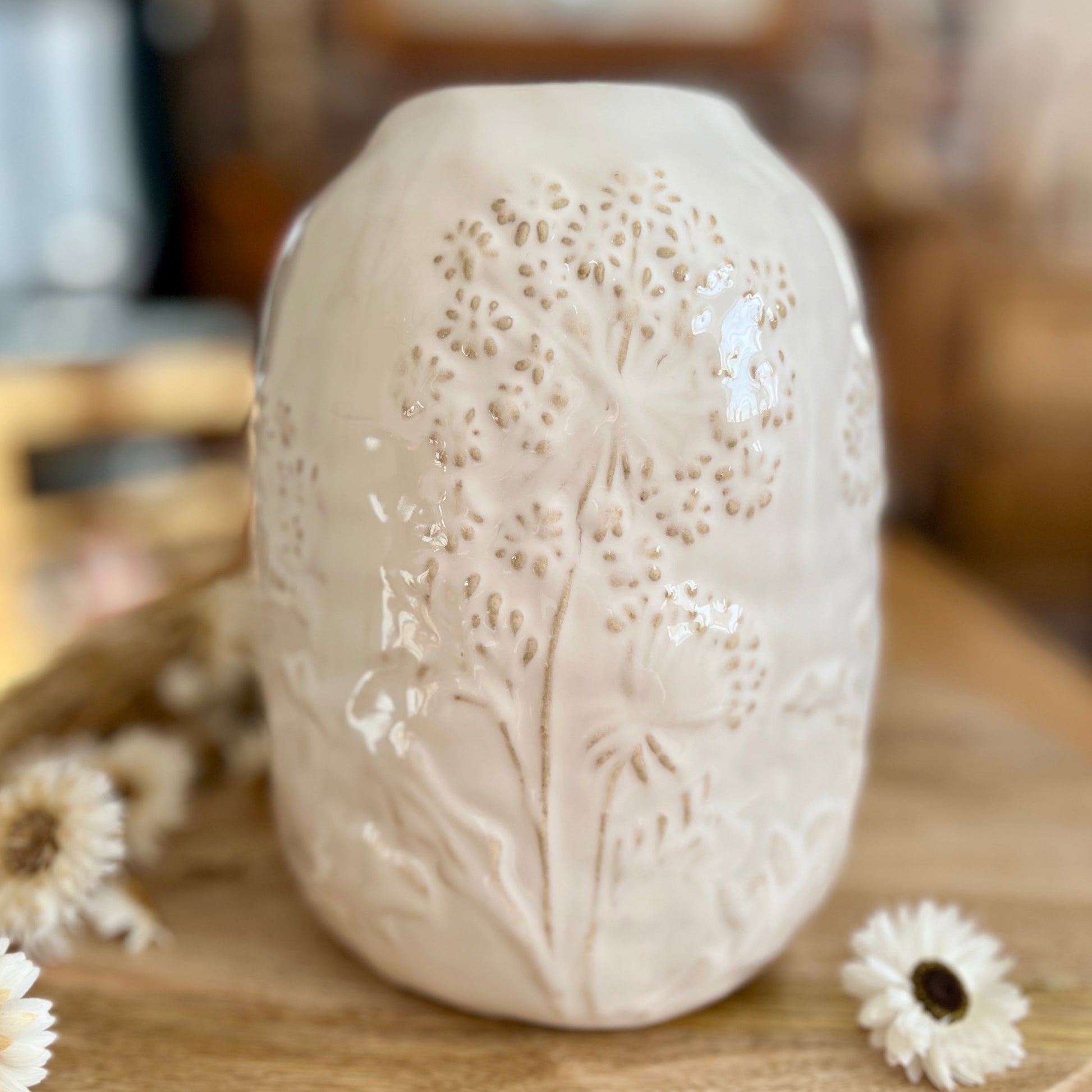 Close up of white ceramic vase with floral patterns on a wooden surface