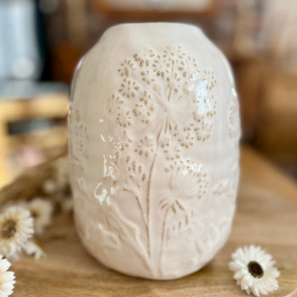 Close up of white ceramic vase with floral patterns on a wooden surface