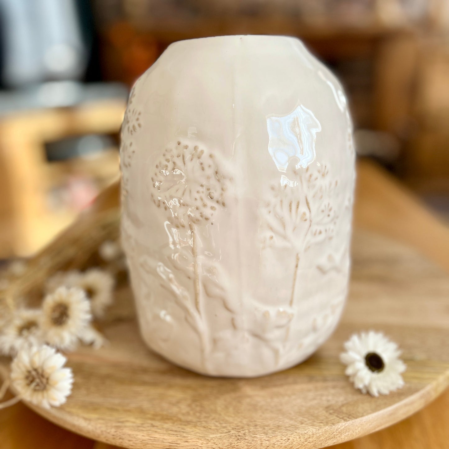 White ceramic jar with floral design on a wooden surface with dried flowers.