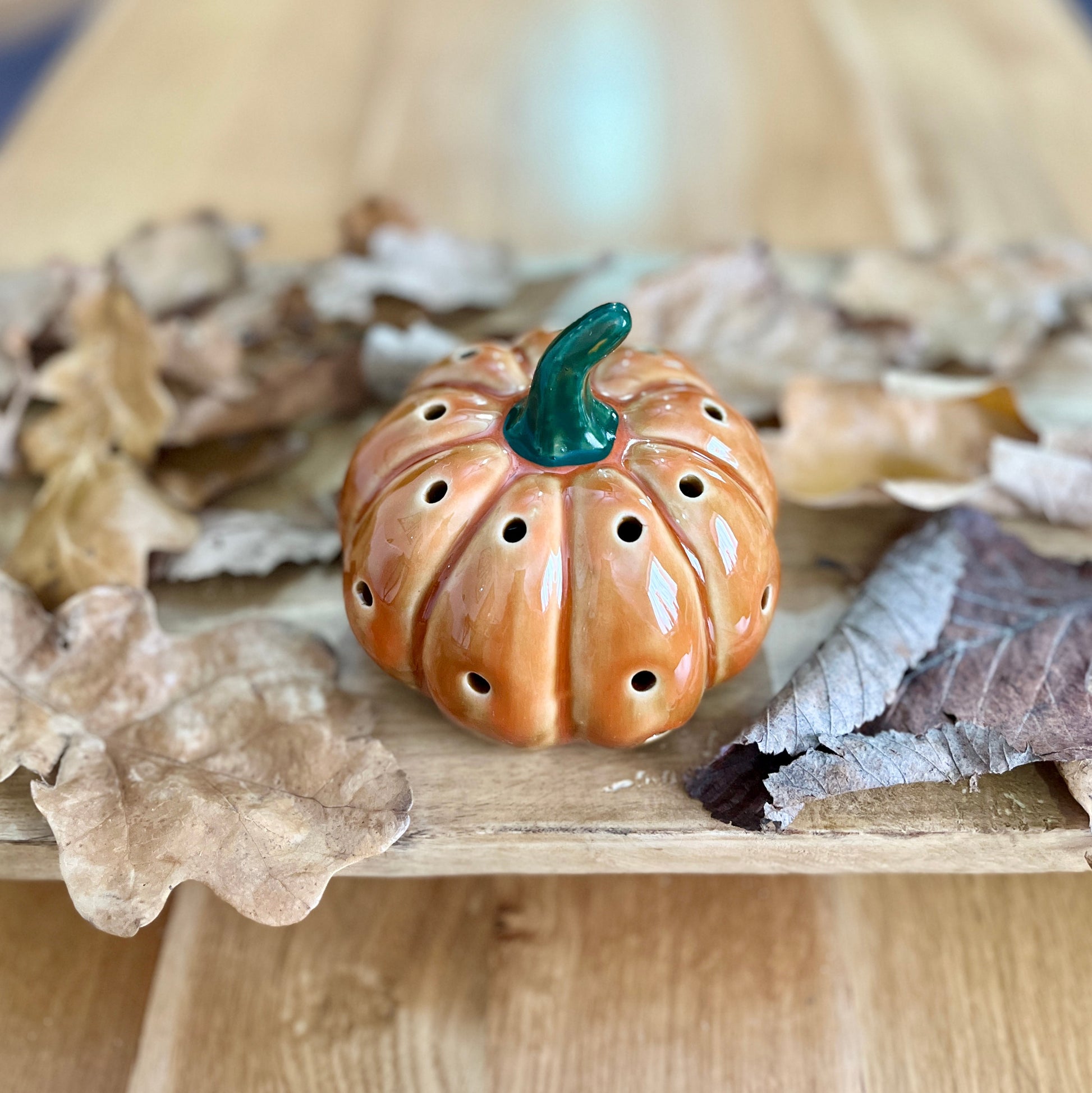 Ceramic pumpkin shaped decorative ornament on a wooden surface with leaves