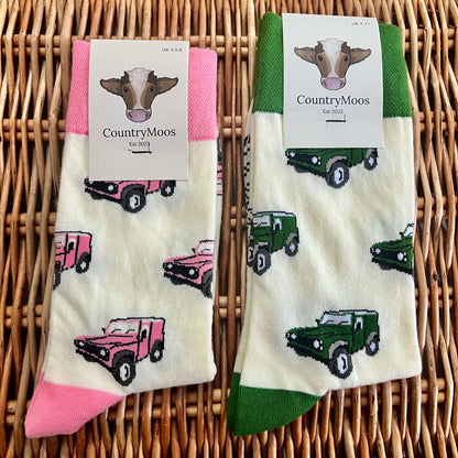 Two pairs of socks with Land Rover patterns (one pink, one green) on a wicker surface, featuring 'Country Moos' branding.