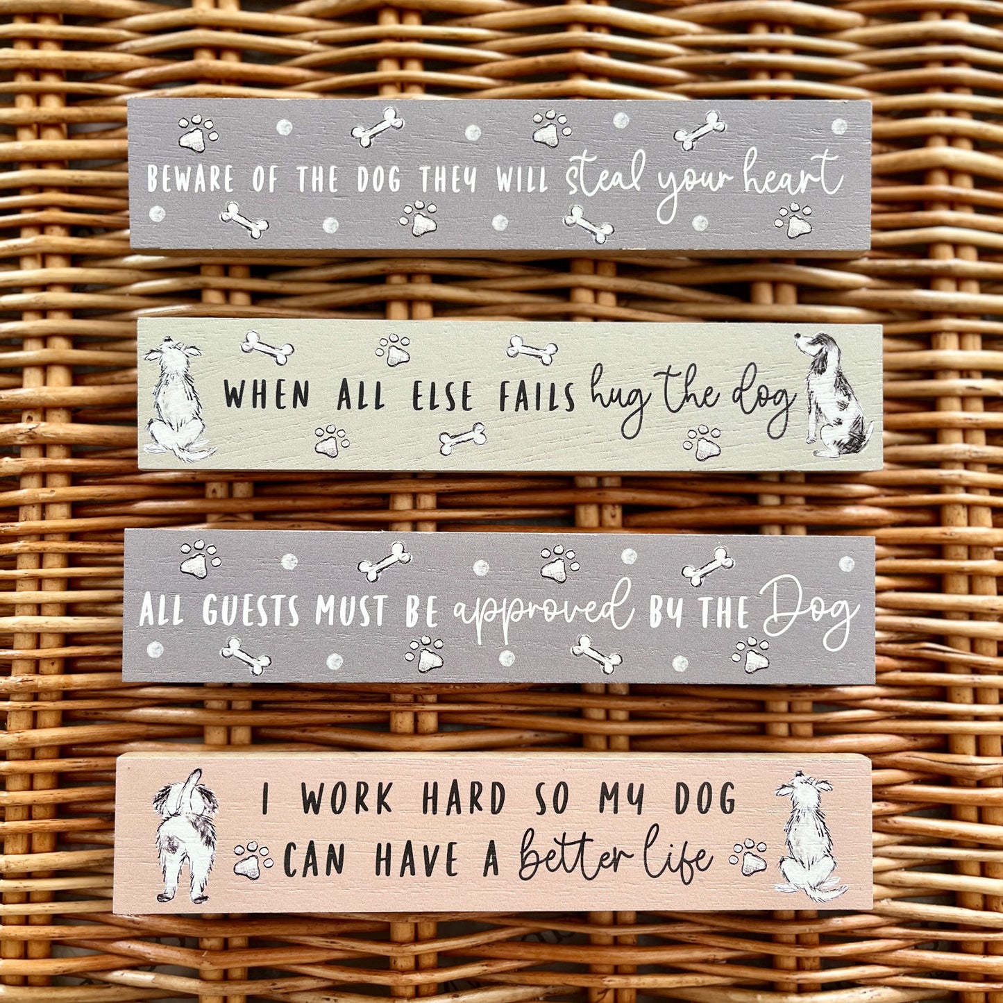 Four wooden signs with dog-themed sayings on a wicker background