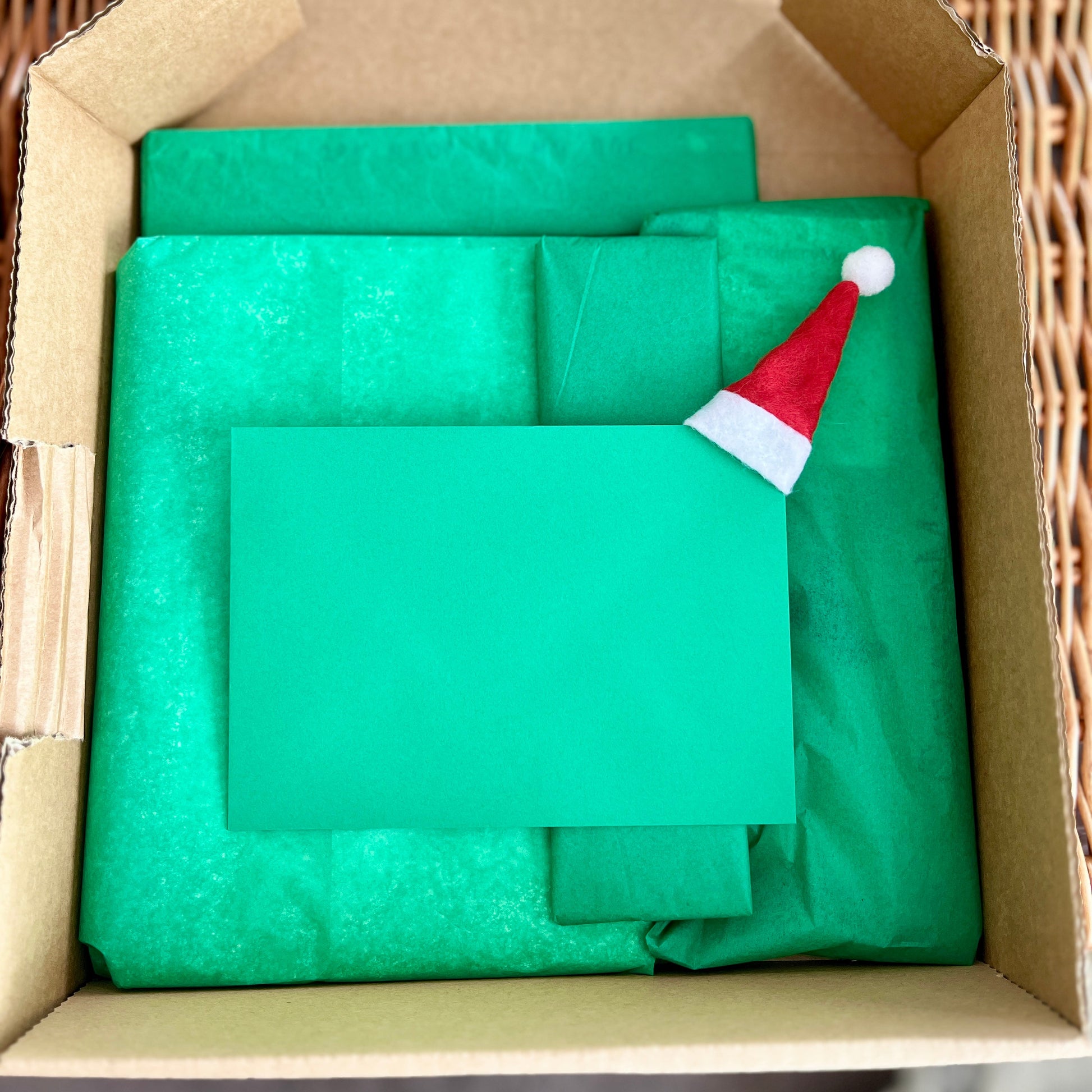 Green paper and a Santa hat in an open cardboard box
