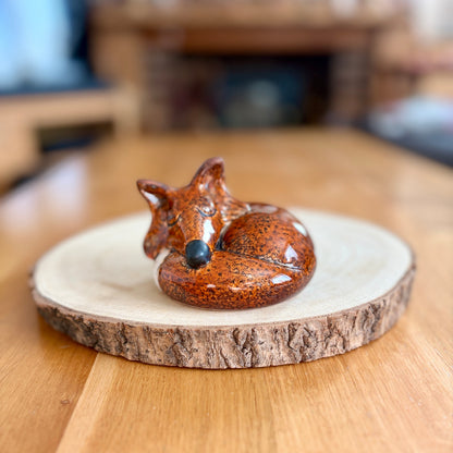 Ceramic fox figurine on a wooden coaster with a blurred background