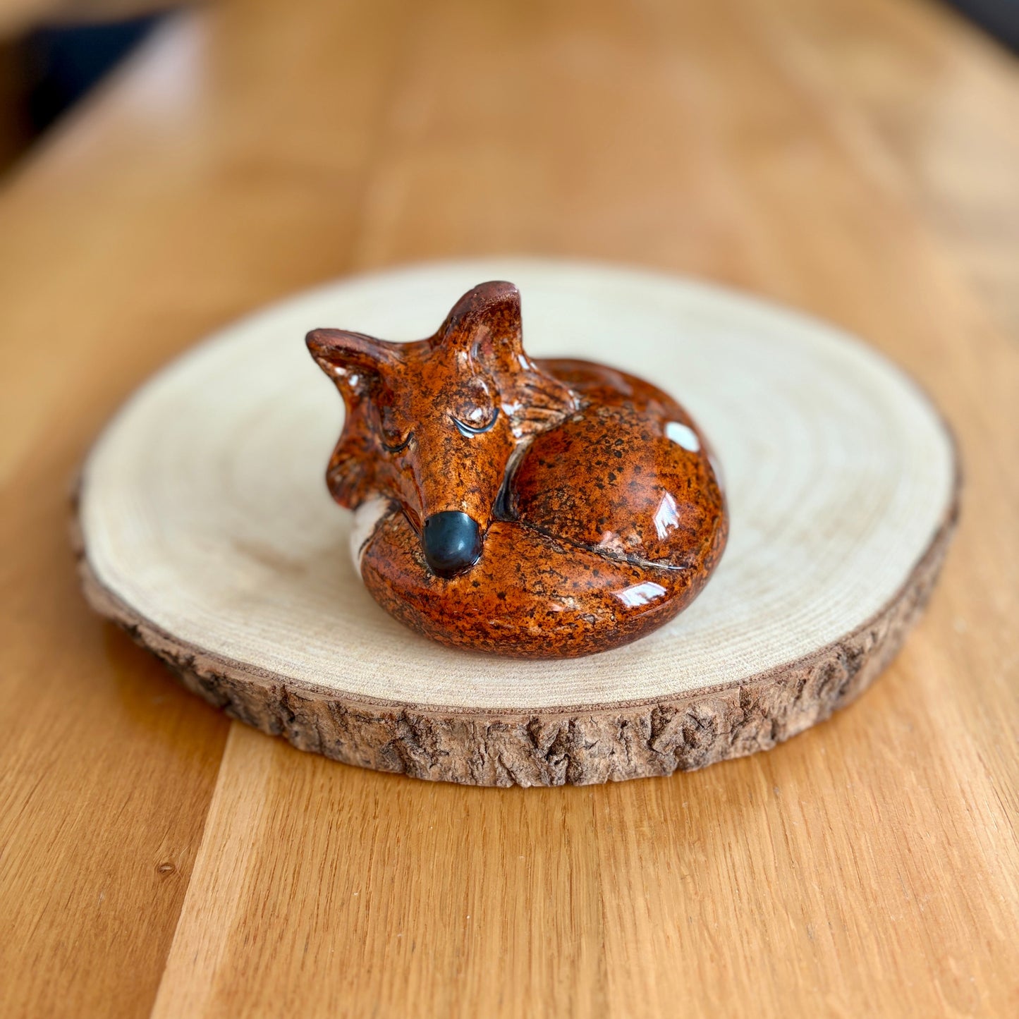 Ceramic sleeping fox figurine on a wooden base