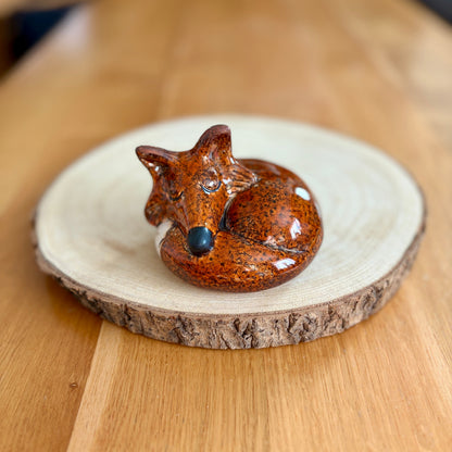 Ceramic sleeping fox figurine on a wooden base