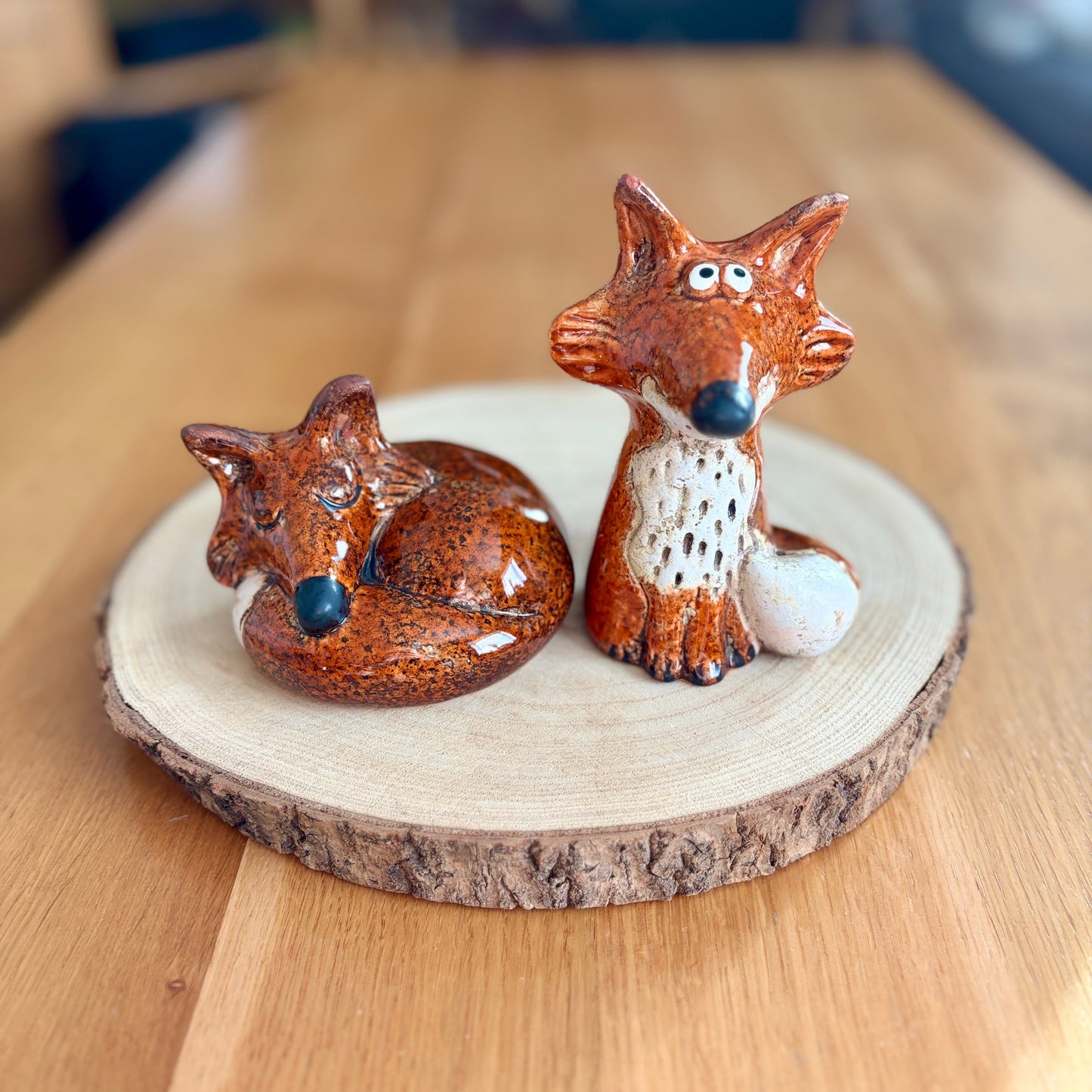 Two ceramic fox figurines on a wooden board with a blurred background