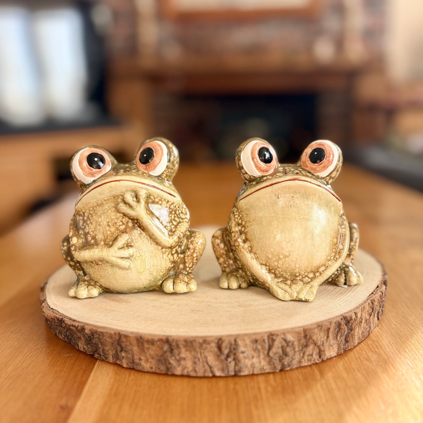 Two frog figurines on a wooden base with a blurred indoor background