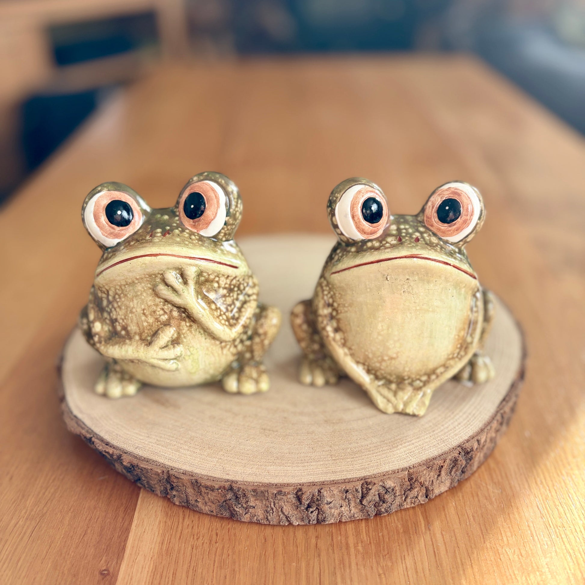 Two green frog figurines on a wooden stand with a blurred background