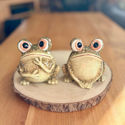 Two green frog figurines on a wooden stand with a blurred background