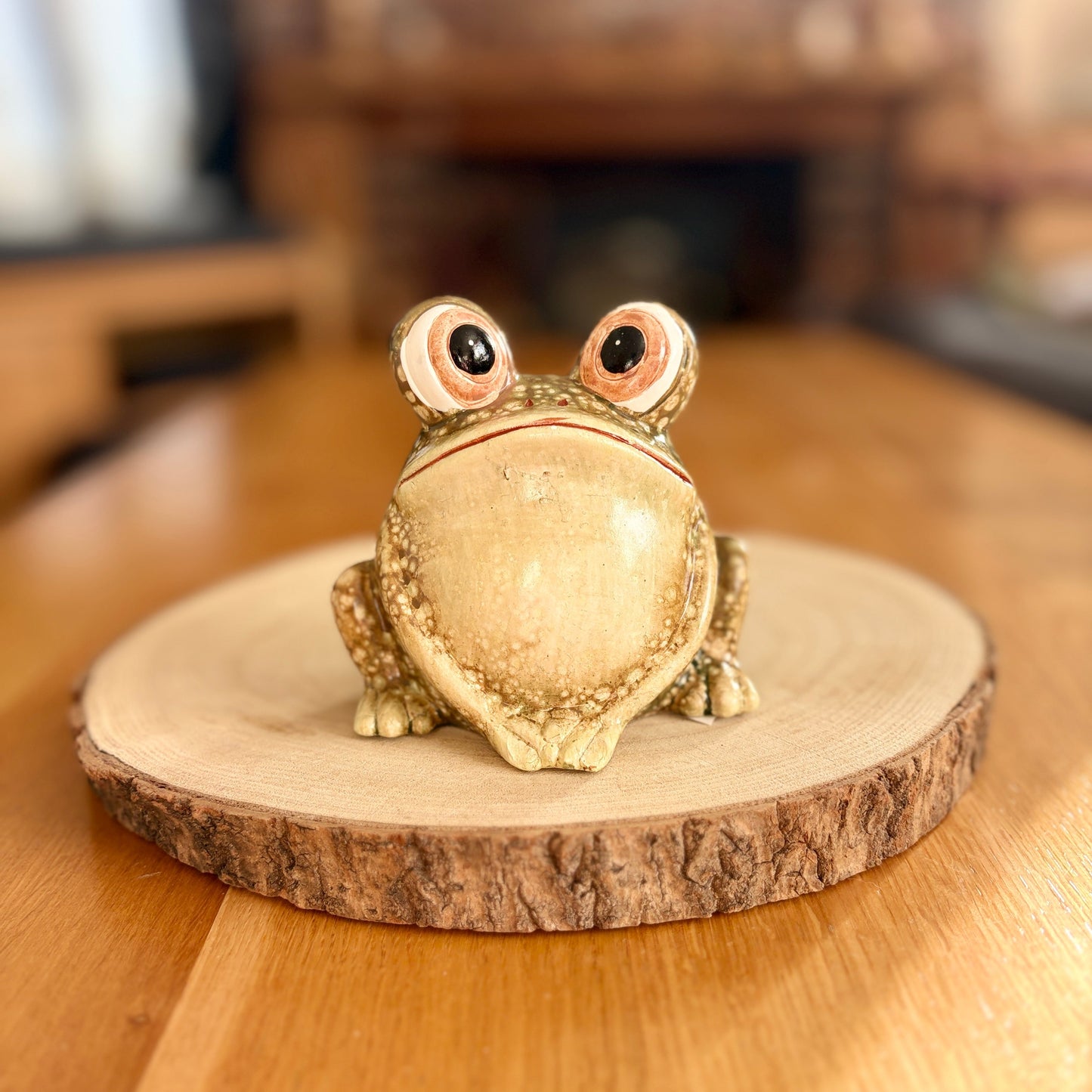 Decorative frog figurine on a wooden stand with a blurred indoor background