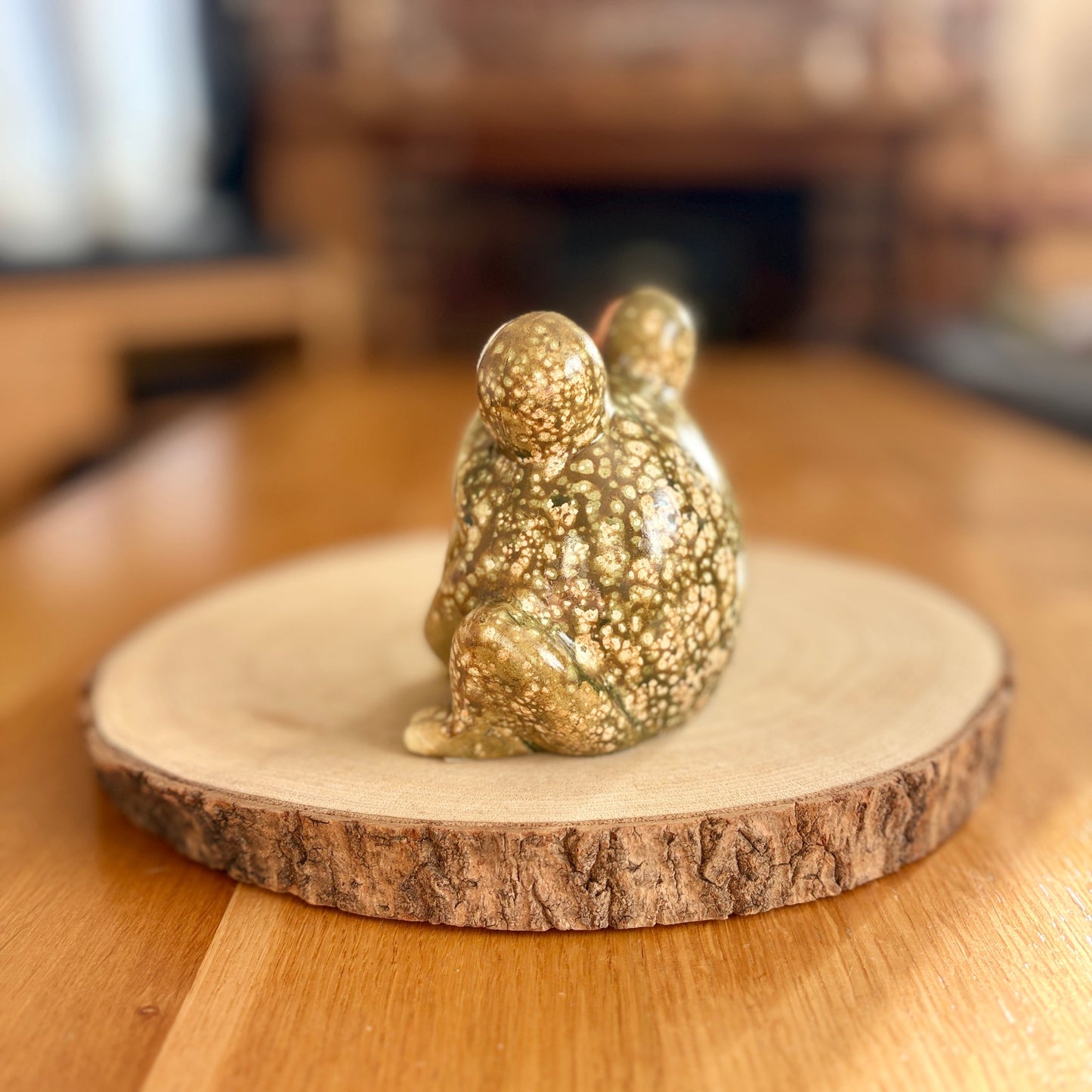 Decorative frog figurine from the back on a wooden stand with a blurred indoor background