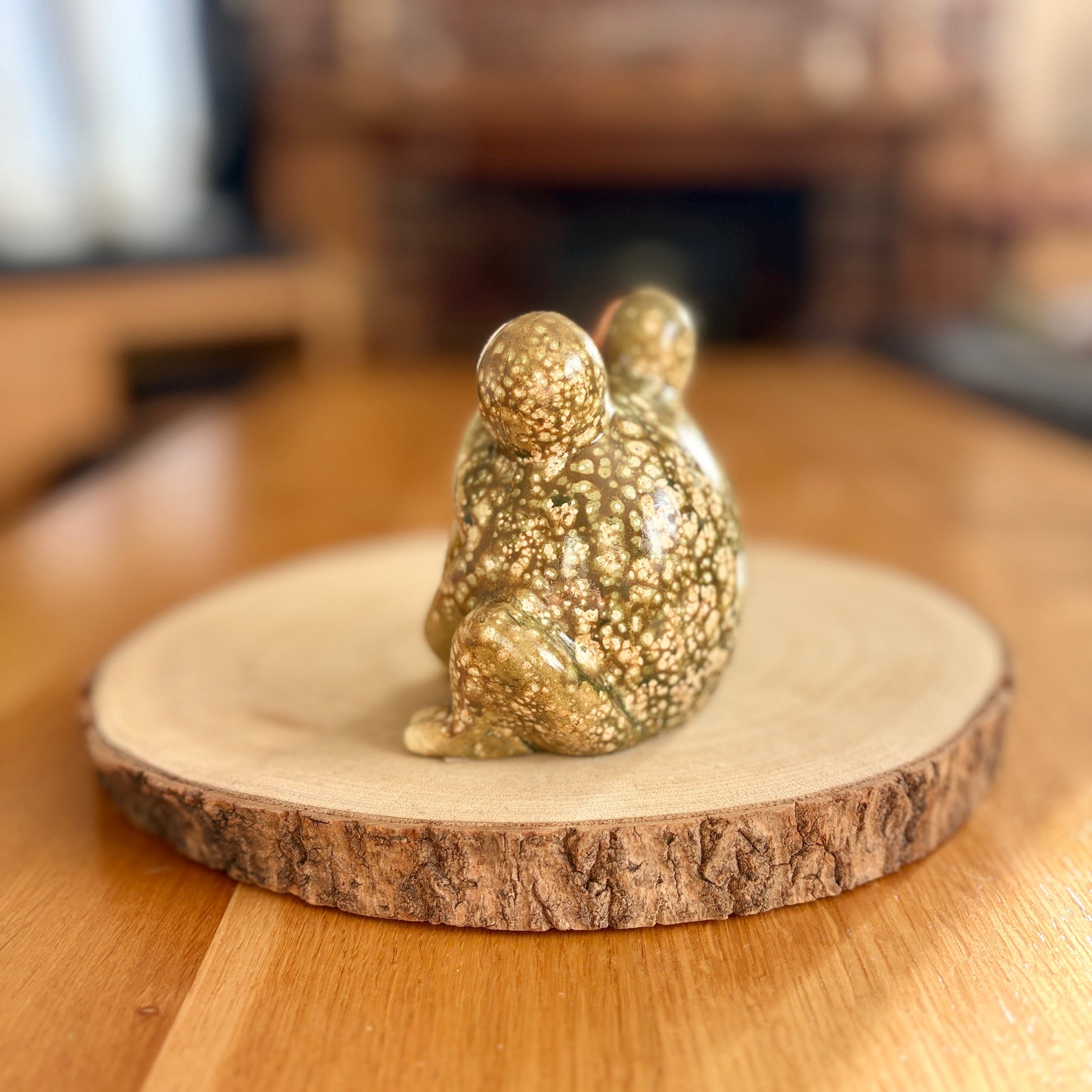 Decorative frog figurine from the back on a wooden stand with a blurred indoor background