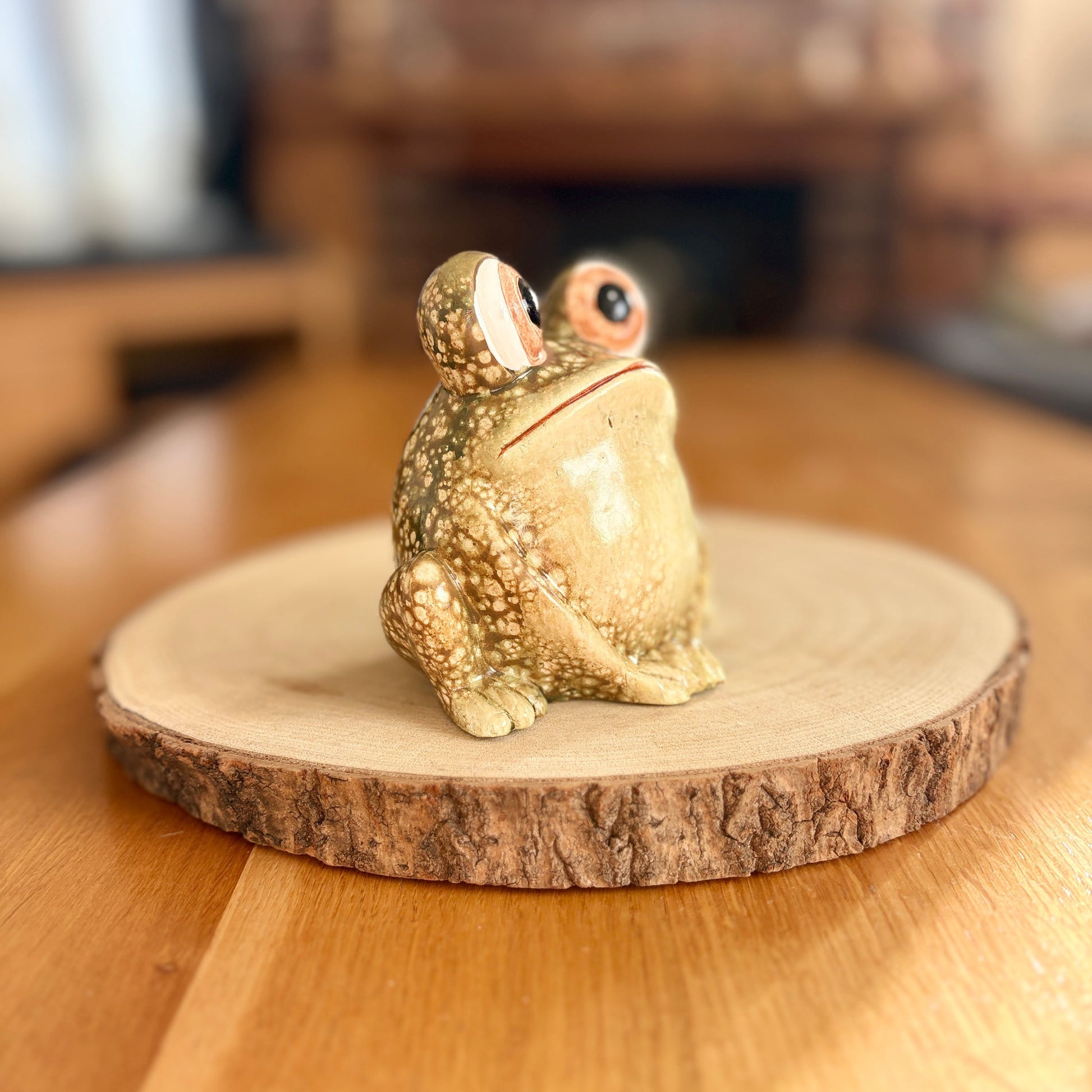 Decorative frog figurine on a wooden base with a blurred indoor background