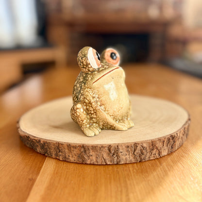 Decorative frog figurine on a wooden base with a blurred indoor background