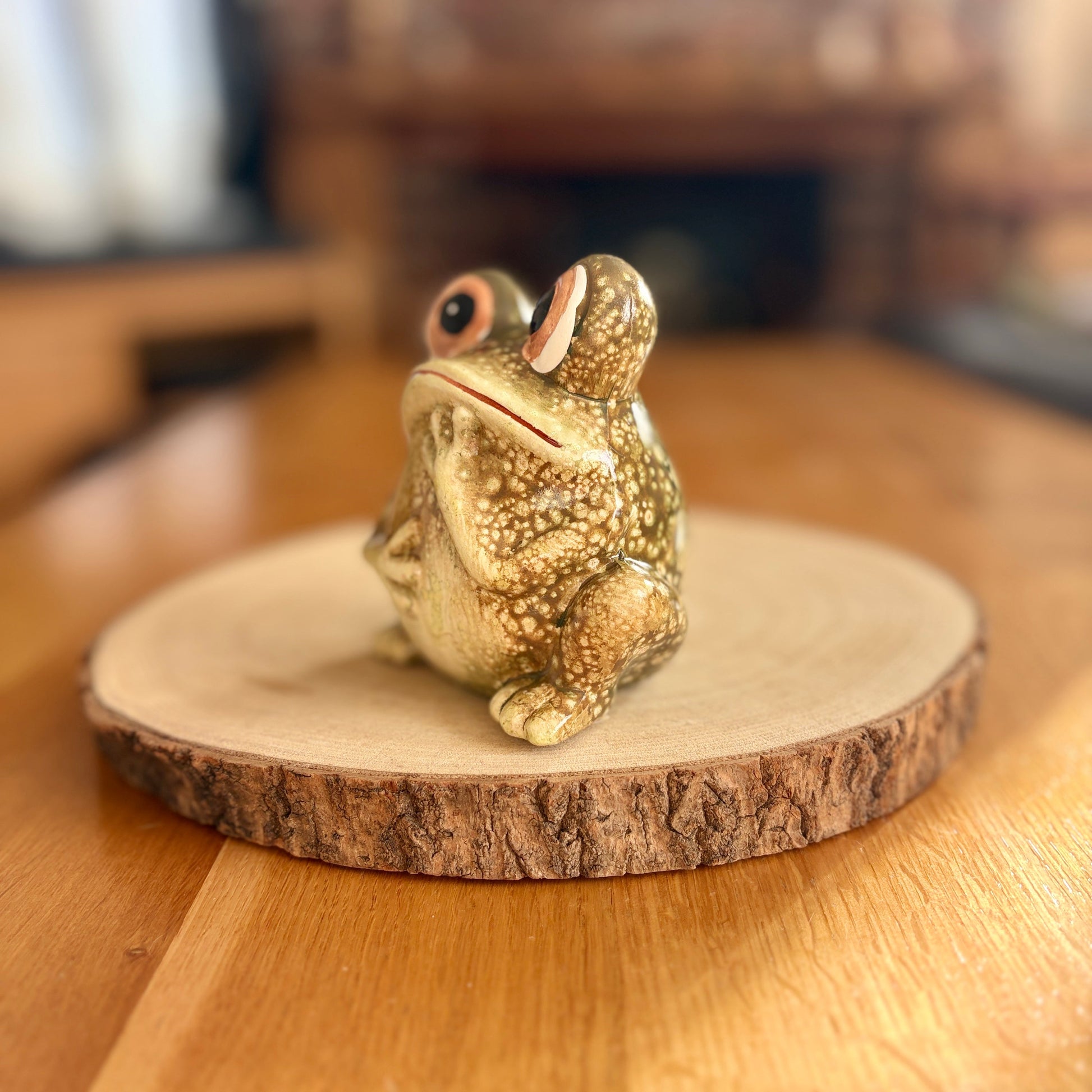 Frog figurine on a wooden base with a blurred indoor background