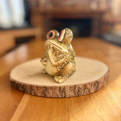 Frog figurine on a wooden base with a blurred indoor background