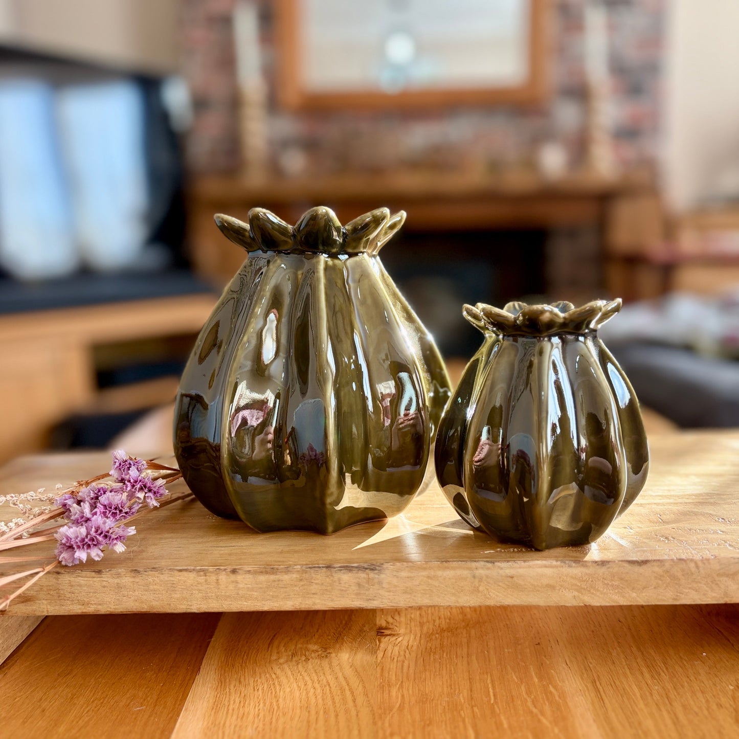 Two green ceramic vases on a wooden surface with a blurred indoor background