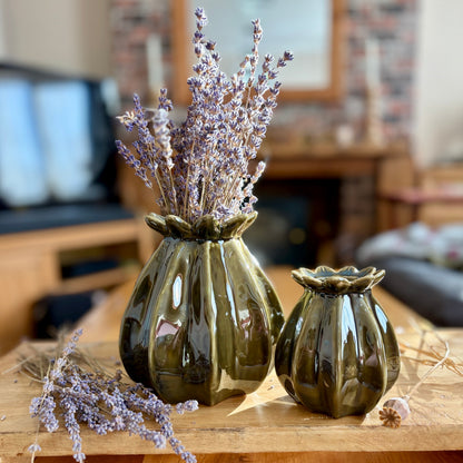 Two green ceramic vases in the shape of poppy seeds with dried lavender on a wooden surface.