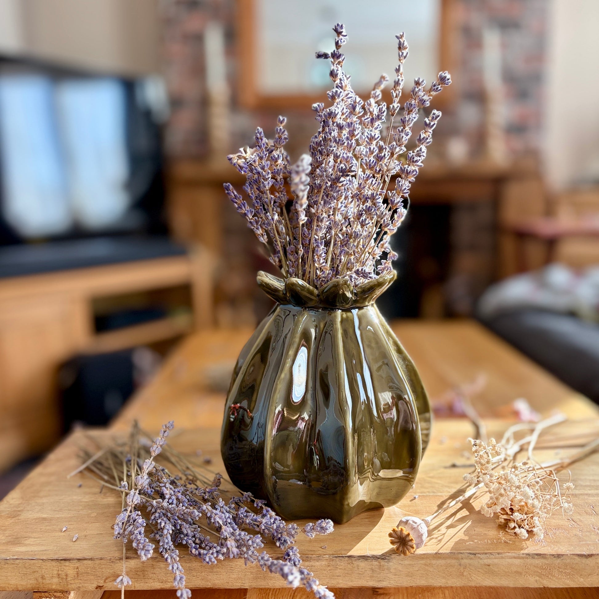 Decorative poppy seed vase with dried lavender on a wooden table in a living room setting.