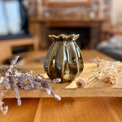 Emerald decorative poppy seed head vase on a wooden surface with dried flowers