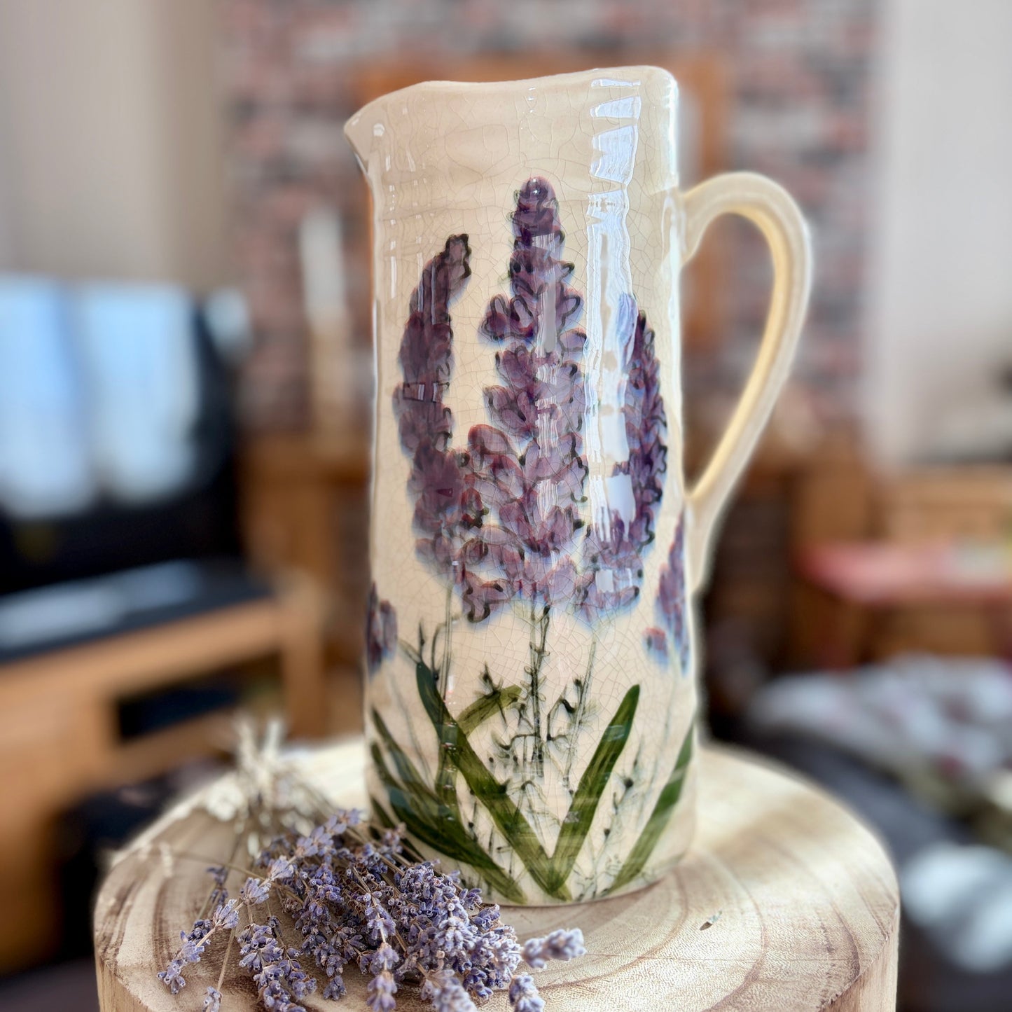Ceramic jug with lavender design on a wooden stand in a blurred indoor setting