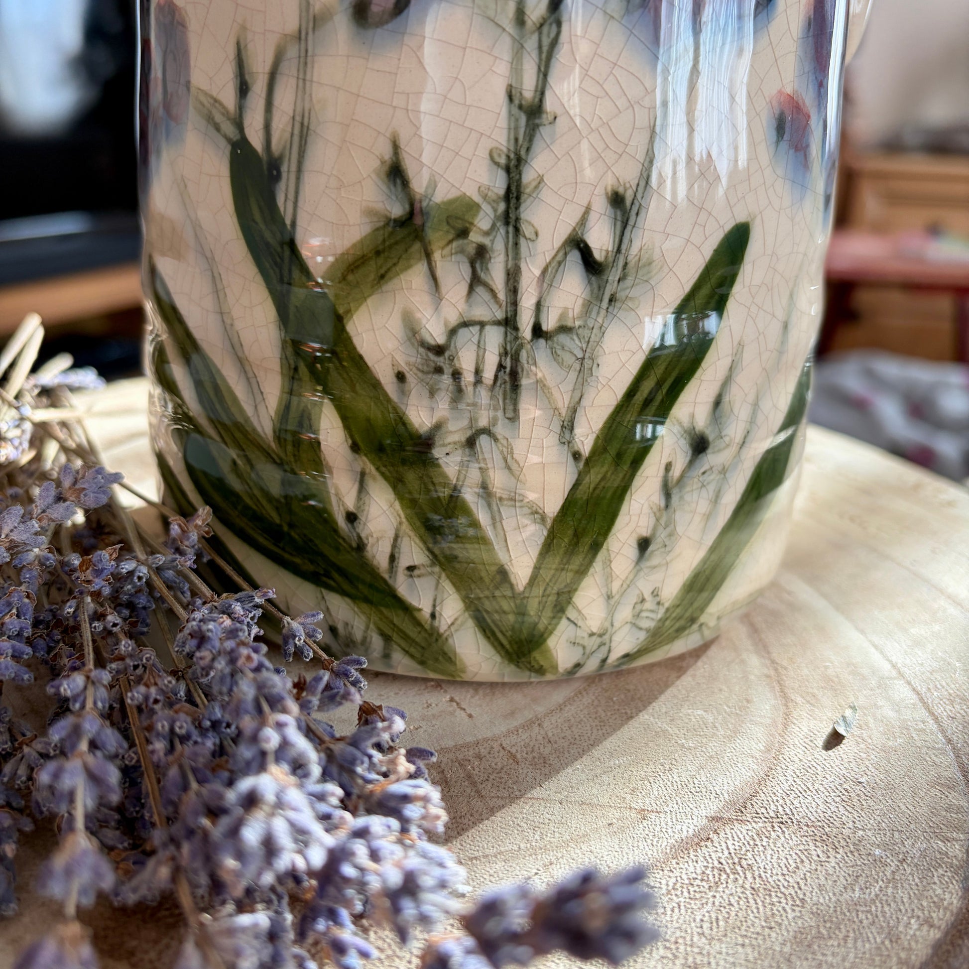 Ceramic vase with floral design on a wooden surface with lavender flowers.
