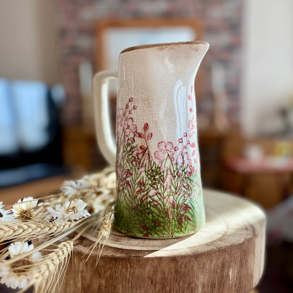 Decorative jug- front view -  with floral design on a wooden stool in a blurred indoor setting
