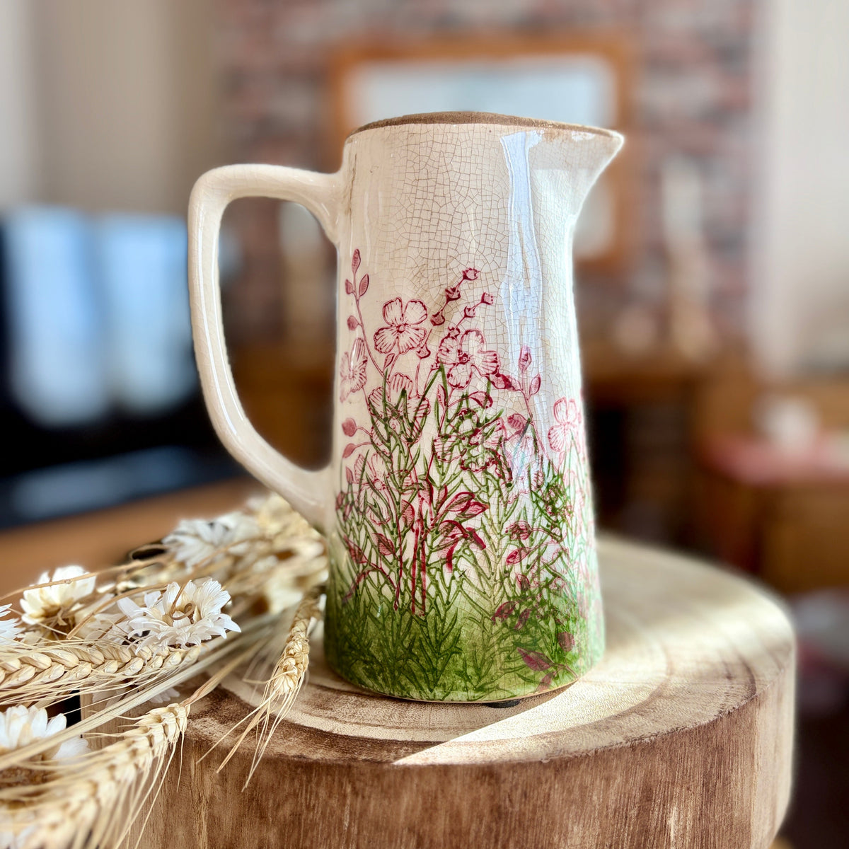 Decorative jug with floral design on a wooden stool in a blurred home setting
