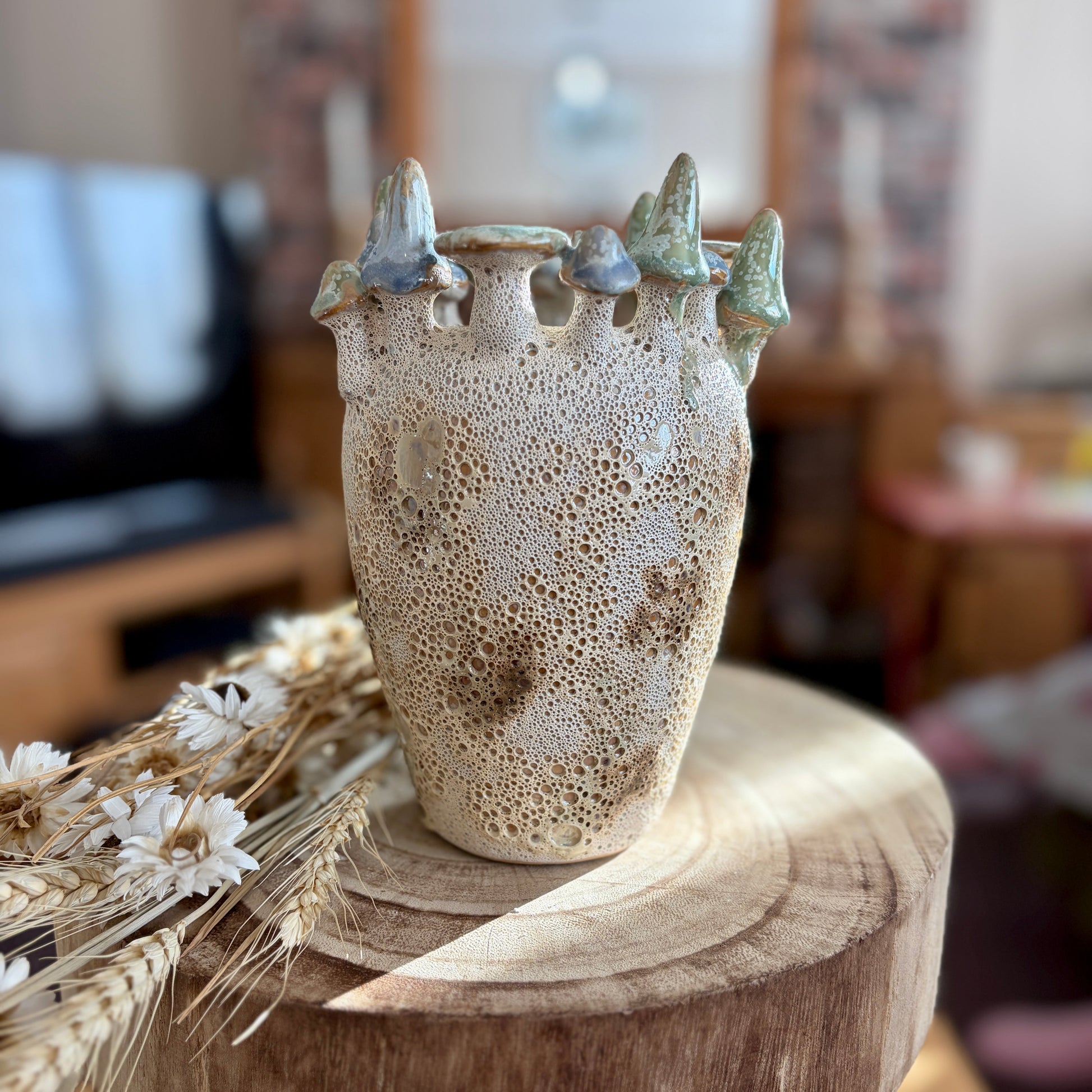 Ceramic vase with textured surface and decorative mushrooms on a wooden stool in a home setting.