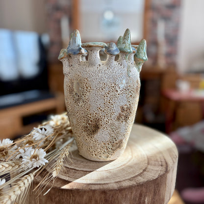 Ceramic vase with textured surface and decorative mushrooms on a wooden stool in a home setting.