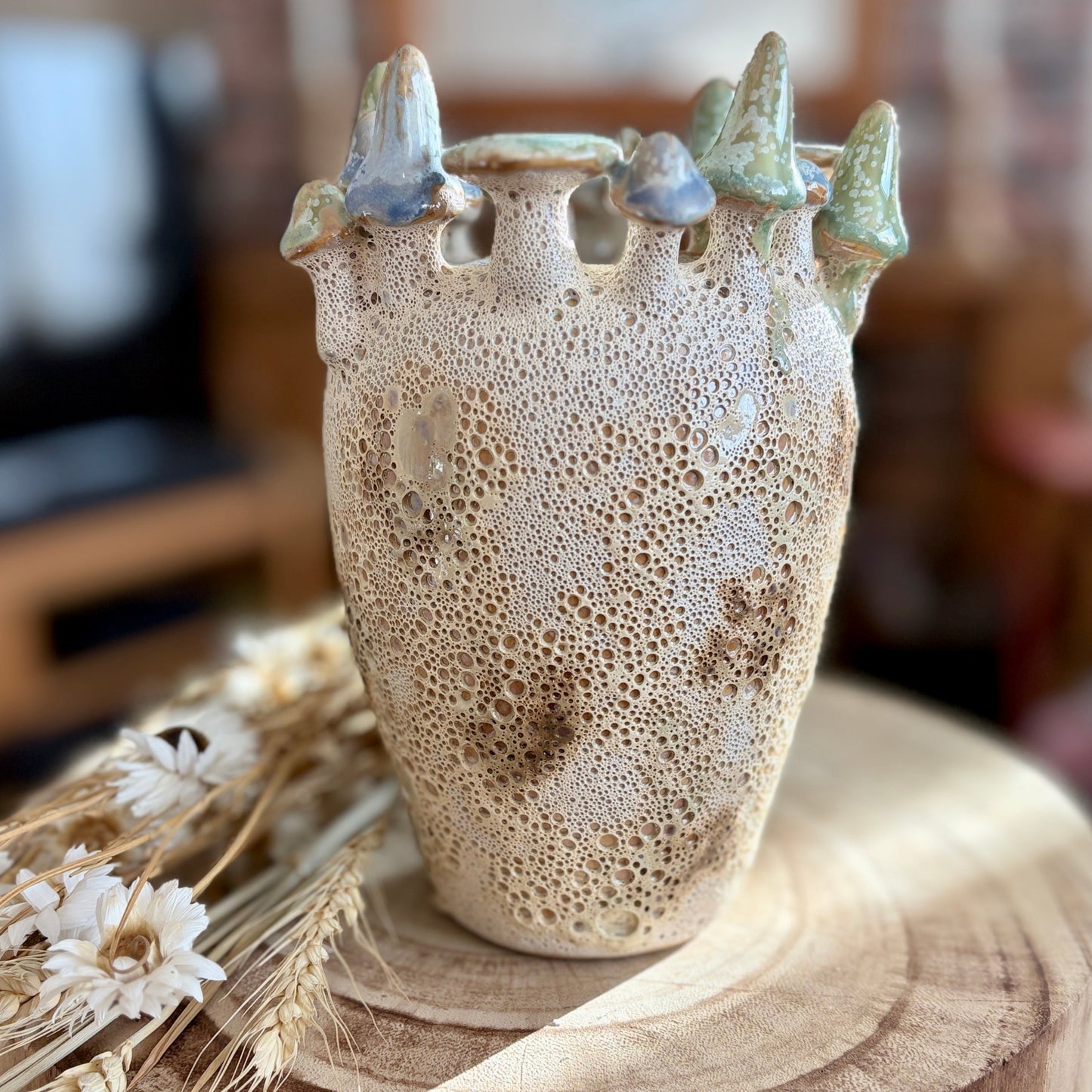 Ceramic vase with textured surface and decorative toadstools on a wooden stool.