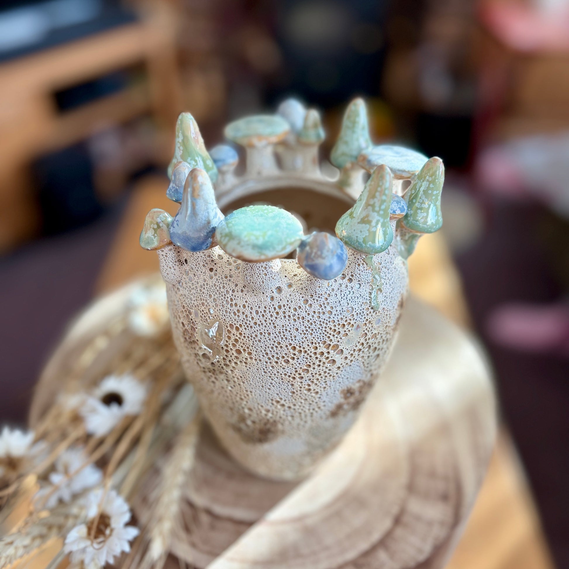 Decorative vase with a textured surface and small mushrooms on top, set against a blurred home background.