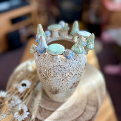 Decorative vase with a textured surface and small mushrooms on top, set against a blurred home background.