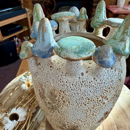 Ceramic vase with textured surface and decorative toadstools on a table with flowers.