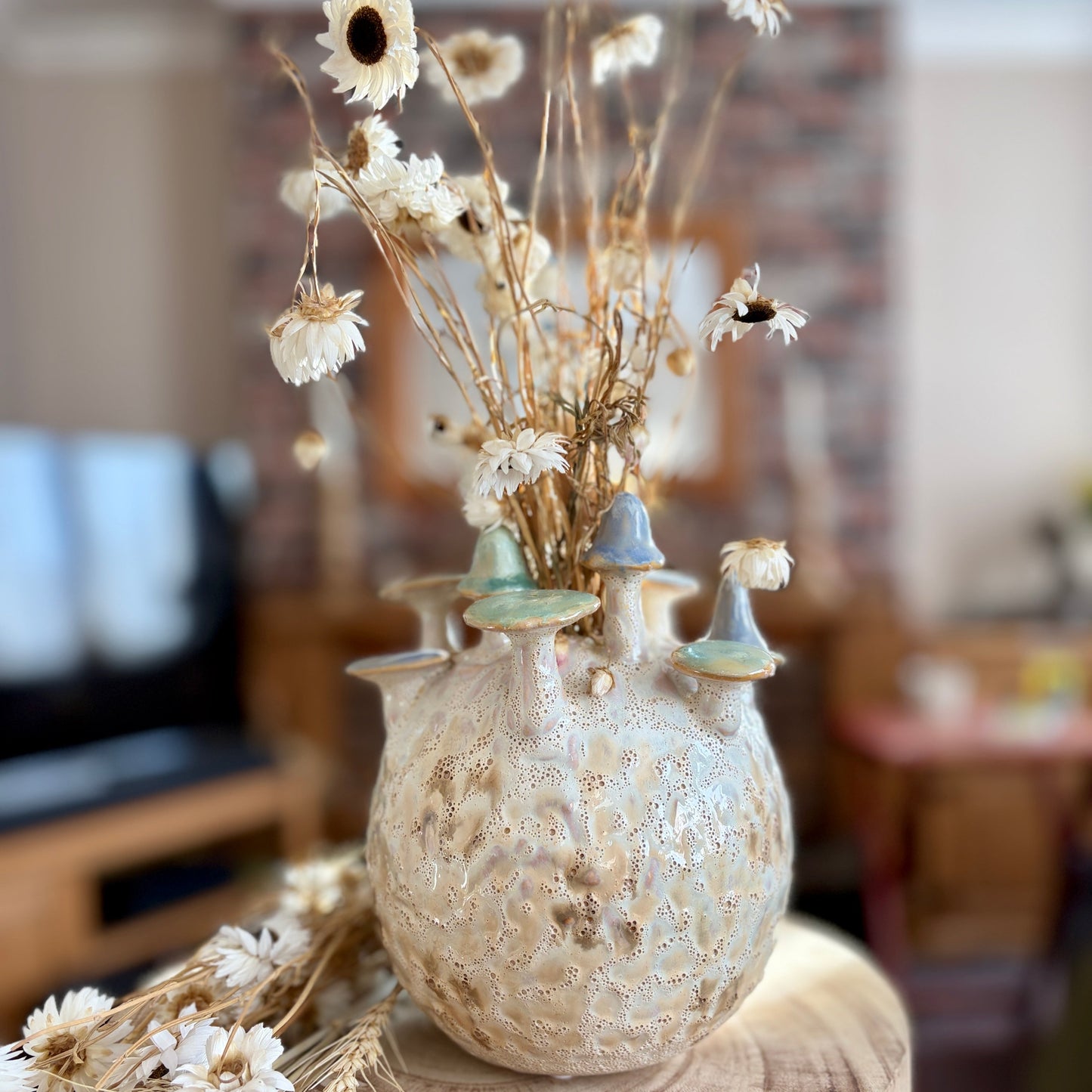 Decorative vase with dried flowers on a wooden surface in a blurred home setting