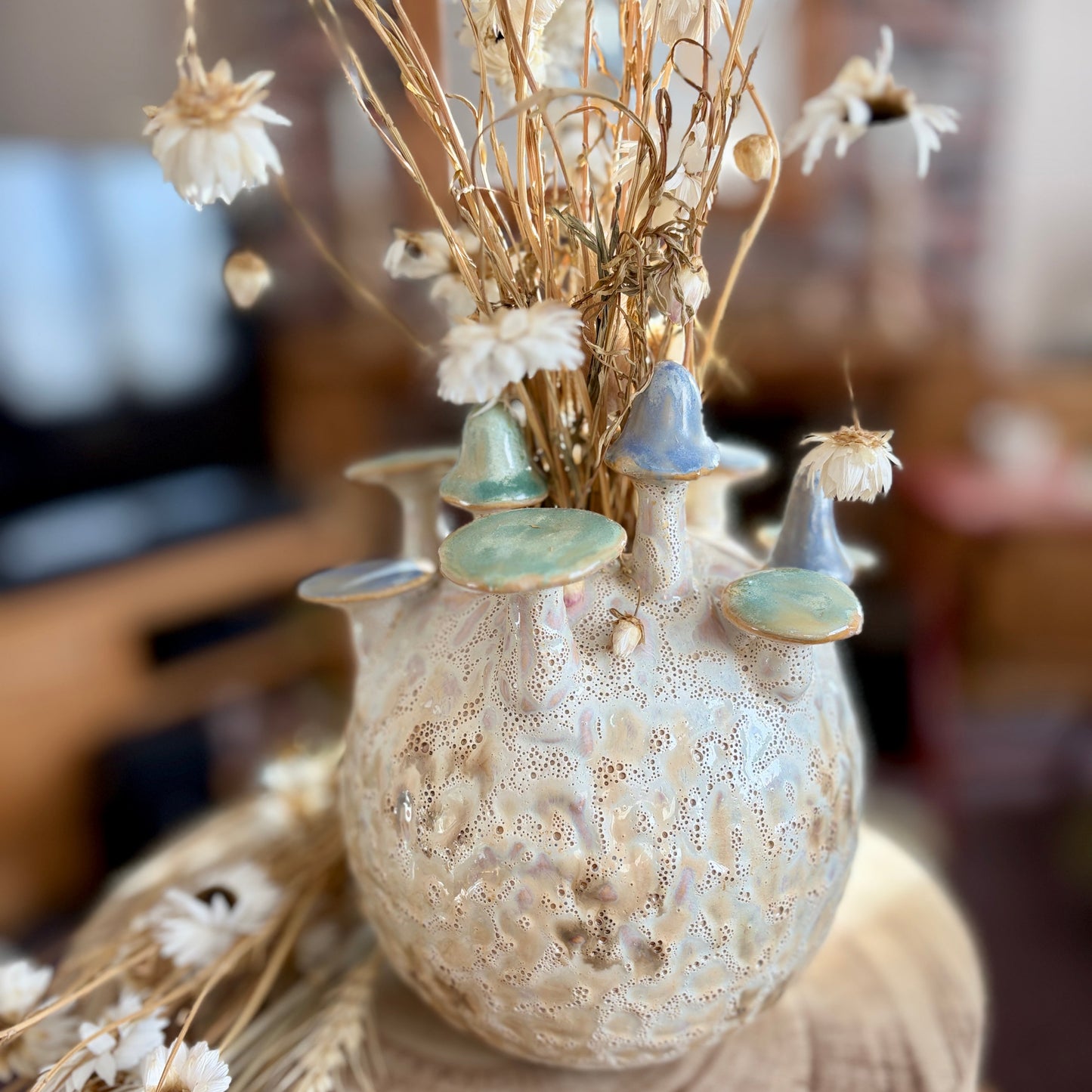 Decorative vase with mushrooms and dried flowers on a wooden surface
