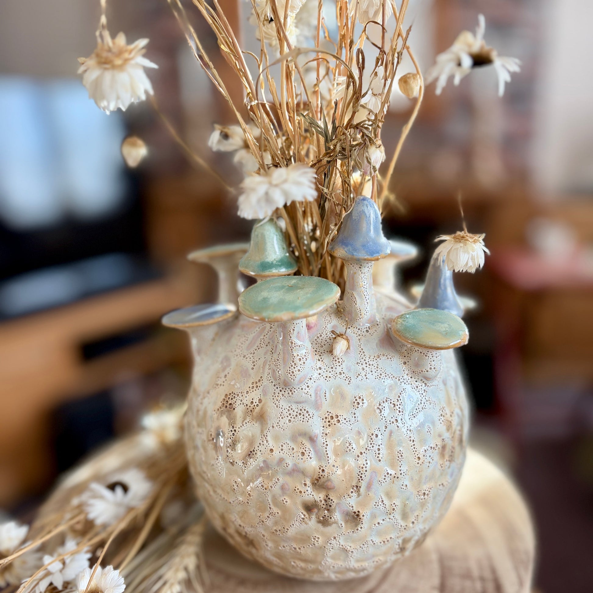 Decorative vase with mushrooms and dried flowers on a wooden surface