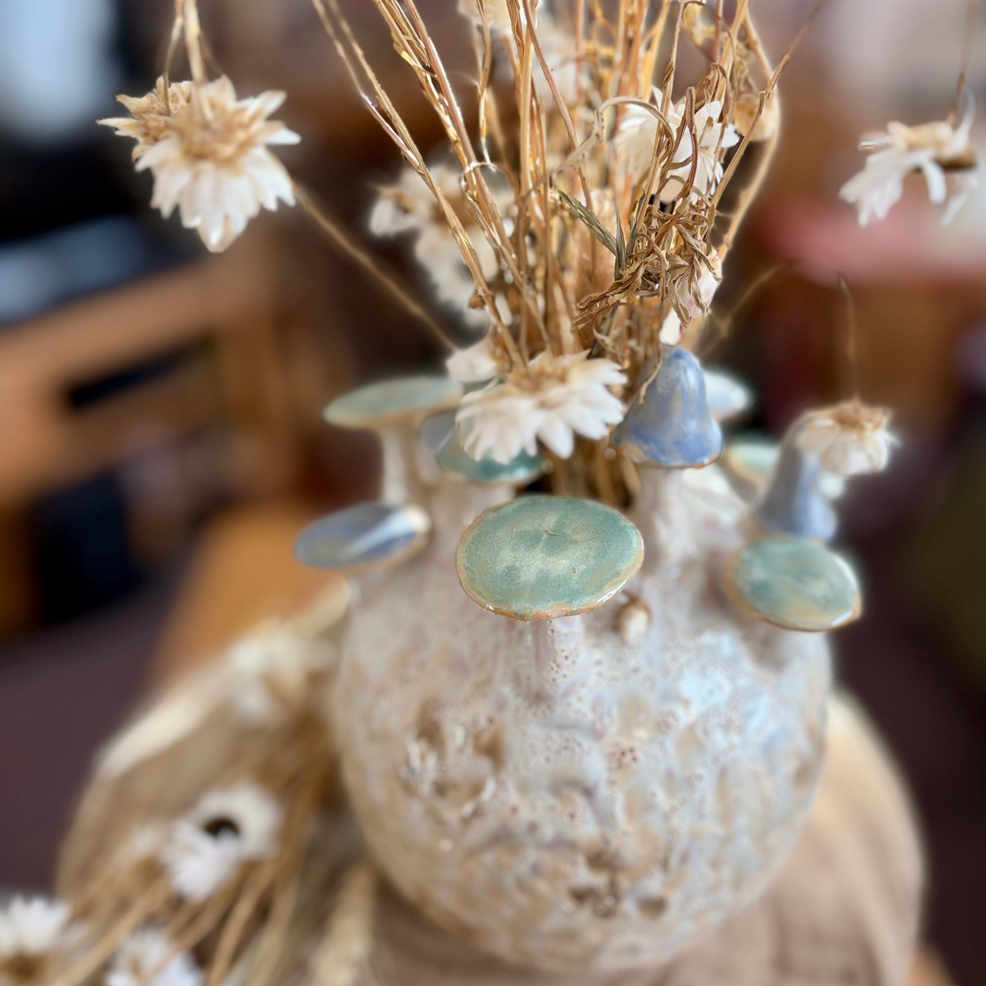 Decorative vase from above with dried flowers and decorative toadstools on a blurred background