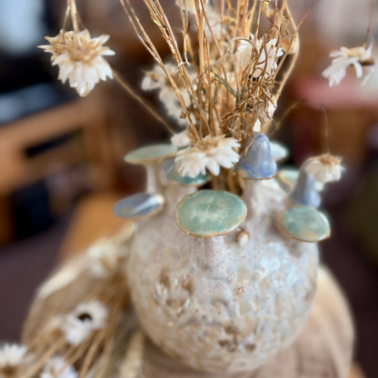 Decorative vase from above with dried flowers and decorative toadstools on a blurred background