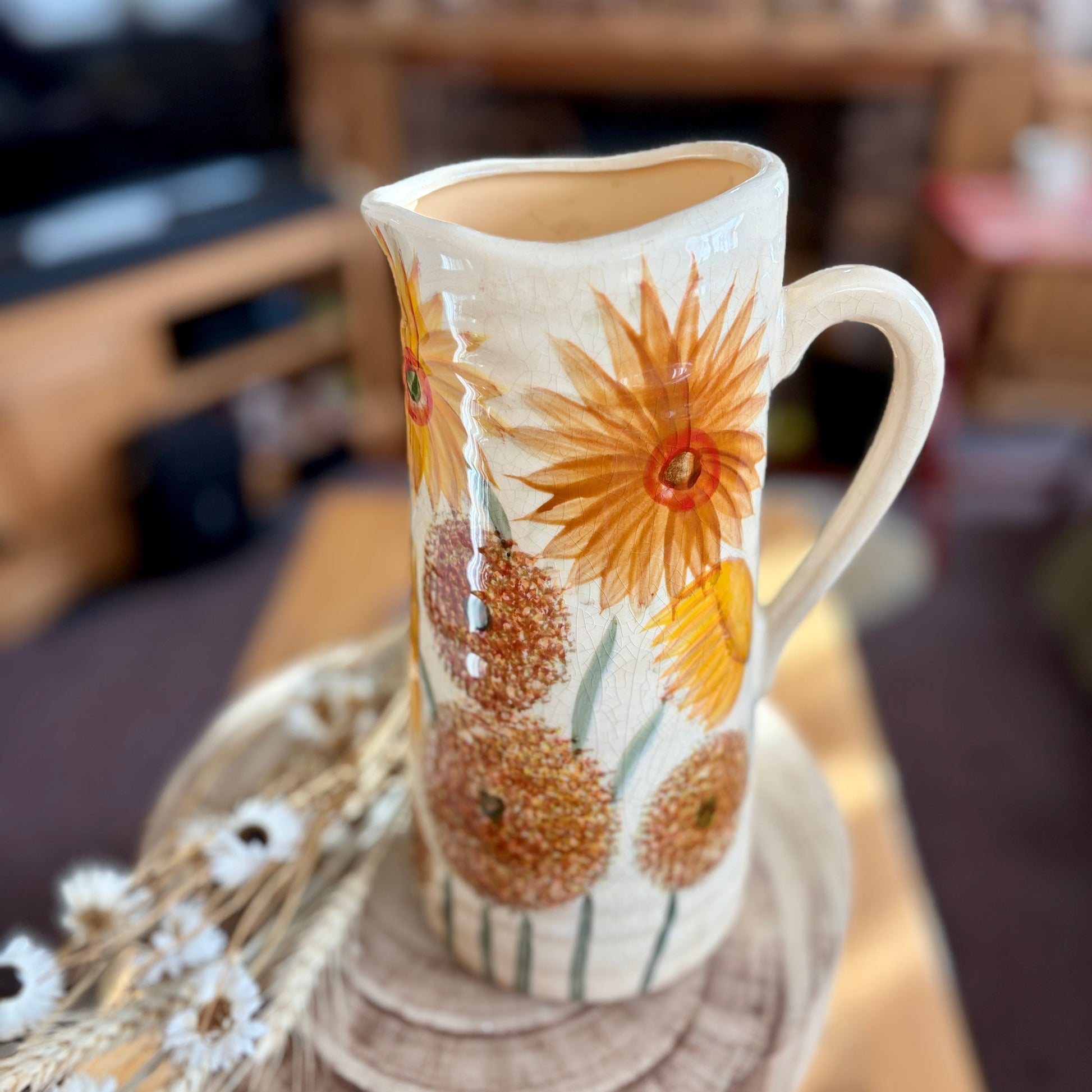 Decorative ceramic jug with bright floral design on a wooden surface stool.