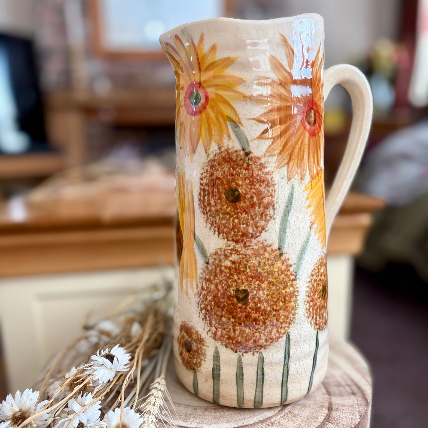 Decorative ceramic jug with sunflower design on a wooden stool.