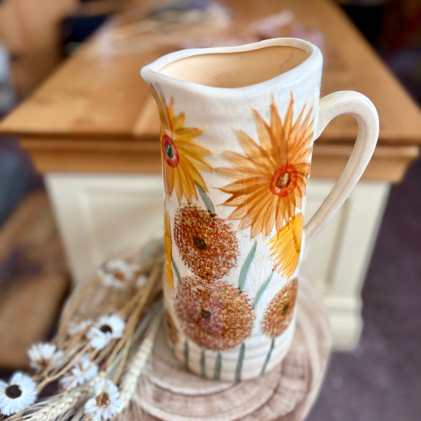 Decorative ceramic jug from above with sunflower design on a wooden stool.